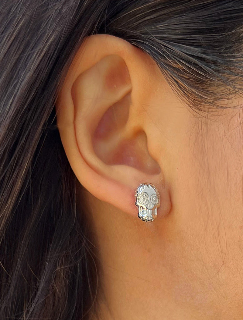 Image Title Woman wearing Culturally inclusive Day Of The Dead Mexican Sugar Skull Stud Earrings in Sterling Silver by Sonia Hou, a celebrity AAPI Chinese demi-fine jewelry designer. This holiday is also known as Dia De Los Muertos, and can also be worn for Halloween!