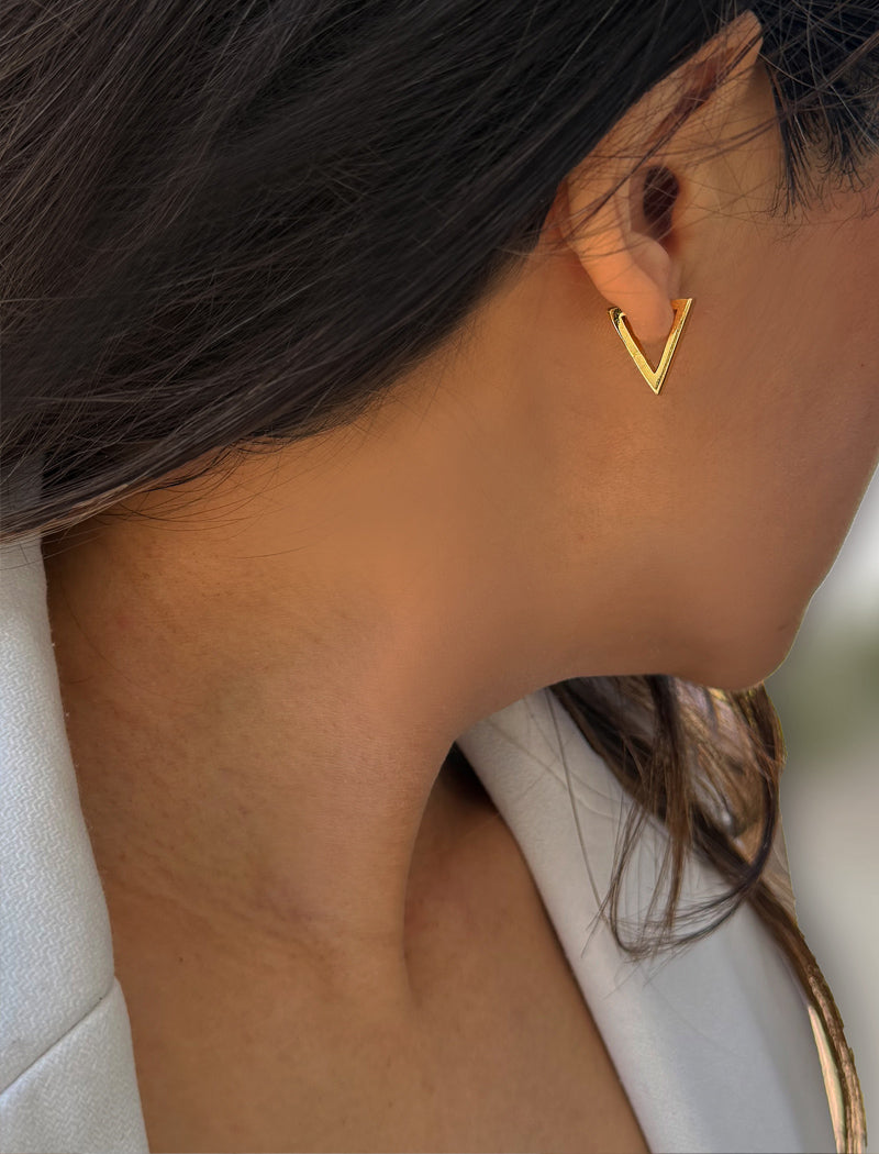 A close-up side profile of a woman wearing a small gold V-shaped hoop earring. ACHIEVE TRIANGLE GEOMETRIC HUGGIE EARRINGS IN 18K GOLD Over Sterling Silver by Sonia Hou Jewelry