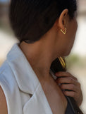 A close-up side profile of a woman wearing a small gold chevron-shaped stud earring, a white sleeveless top, and dark hair. ACHIEVE TRIANGLE GEOMETRIC HUGGIE EARRINGS IN 18K GOLD Over Sterling Silver by Sonia Hou Jewelry