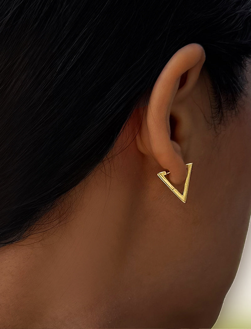 A close-up side profile of a person's ear wearing a small open triangular gold hoop earring. ACHIEVE TRIANGLE GEOMETRIC HUGGIE EARRINGS IN 18K GOLD Over Sterling Silver by Sonia Hou Jewelry