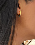 A close-up of a person's ear wearing a small geometric gold hoop earring with a black triangular backing. ACHIEVE TRIANGLE GEOMETRIC HUGGIE EARRINGS IN 18K GOLD Over Sterling Silver by Sonia Hou Jewelry