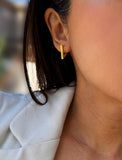 A close-up of a person's ear wearing a small gold hoop earring, with dark hair and a light-colored top visible against a softly blurred background. ACHIEVE TRIANGLE GEOMETRIC HUGGIE EARRINGS IN 18K GOLD Over Sterling Silver by Sonia Hou Jewelry
