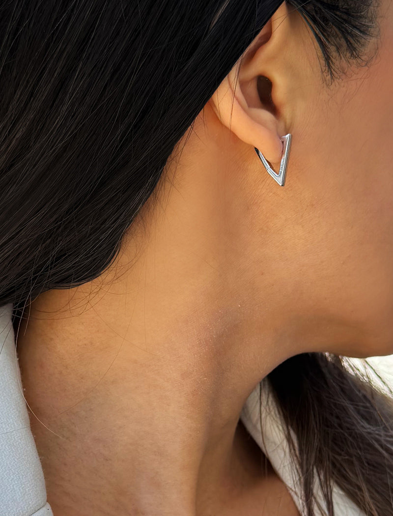 A close-up of a person's ear wearing a small silver geometric triangle stud earring. ACHIEVE TRIANGLE GEOMETRIC HUGGIE EARRINGS IN  Sterling Silver by Sonia Hou Jewelry