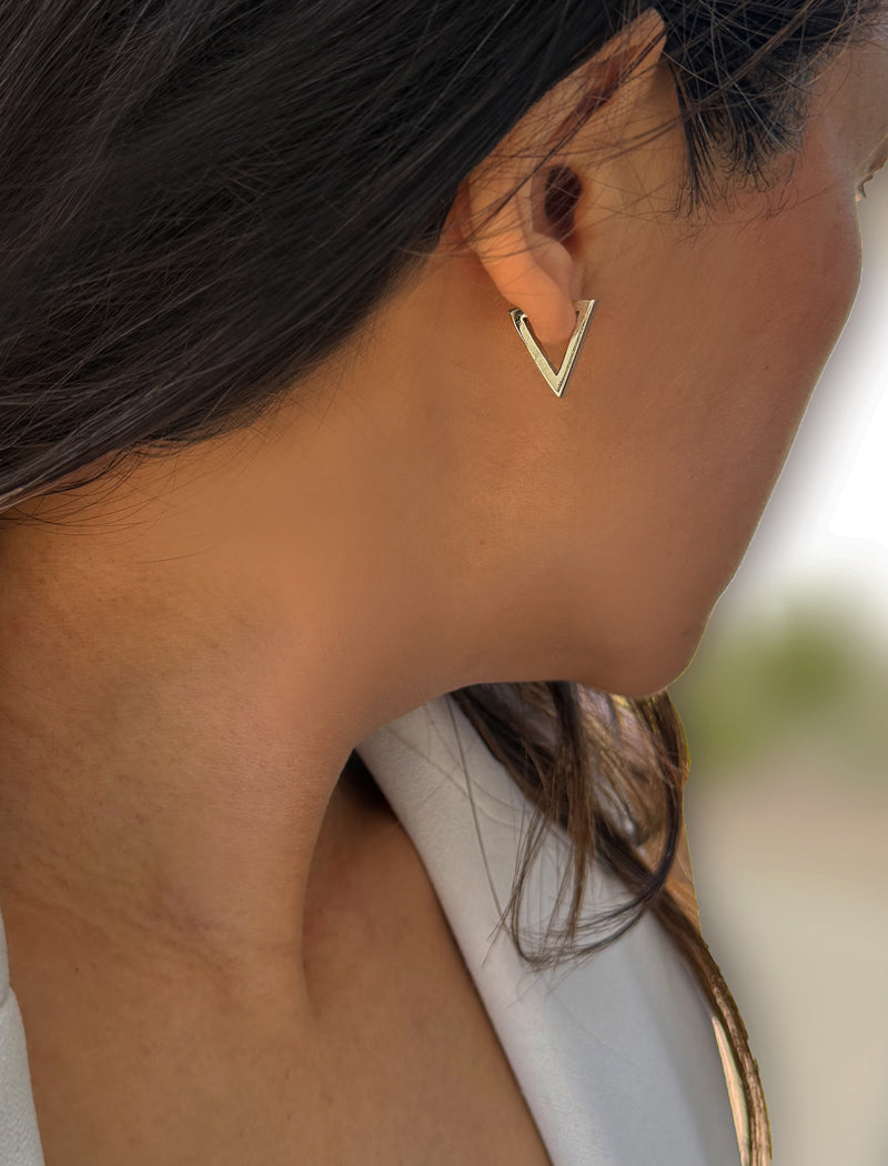 A close-up side profile of a woman wearing a small gold V-shaped stud earring. ACHIEVE TRIANGLE GEOMETRIC HUGGIE EARRINGS IN  Sterling Silver by Sonia Hou Jewelry