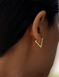 A close-up side profile of a person wearing a small gold triangular hoop earring. ACHIEVE TRIANGLE GEOMETRIC HUGGIE EARRINGS IN  Sterling Silver by Sonia Hou Jewelry