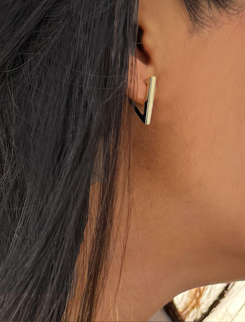 A close-up of a person's ear wearing a modern geometric stud earring with a vertical gold bar and a black triangular accent. ACHIEVE TRIANGLE GEOMETRIC HUGGIE EARRINGS IN  Sterling Silver by Sonia Hou Jewelry