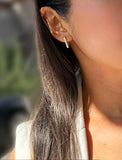 A close-up of a woman's ear wearing a small, minimalist gold geometric stud earring. ACHIEVE TRIANGLE GEOMETRIC HUGGIE EARRINGS IN  Sterling Silver by Sonia Hou Jewelry
