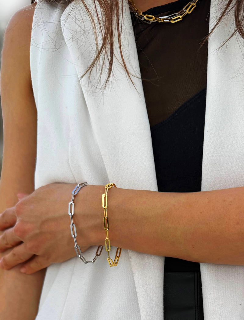 Close-up of a person wearing multiple gold and silver chain bracelets on a white background, 18K Gold vermeil and sterling silver bracelet on a person's wrist with a white blazer and black top. Our medium Essential paperclip link chain bracelet is perfect for everyday wear. Designed by AAPI celebrity jewelry designer SONIA HOU.