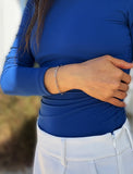A close-up of a person wearing a stainless silver paperclip chain bracelet on their left wrist, paired with a royal blue long-sleeve top and white pants. Designed by AAPI celebrity jewelry designer SONIA HOU.