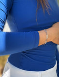 A close-up of a person wearing a stainless steel silver chain link bracelet on their wrist, paired with a royal blue long-sleeve top and white pants. Designed by AAPI celebrity jewelry designer SONIA HOU.