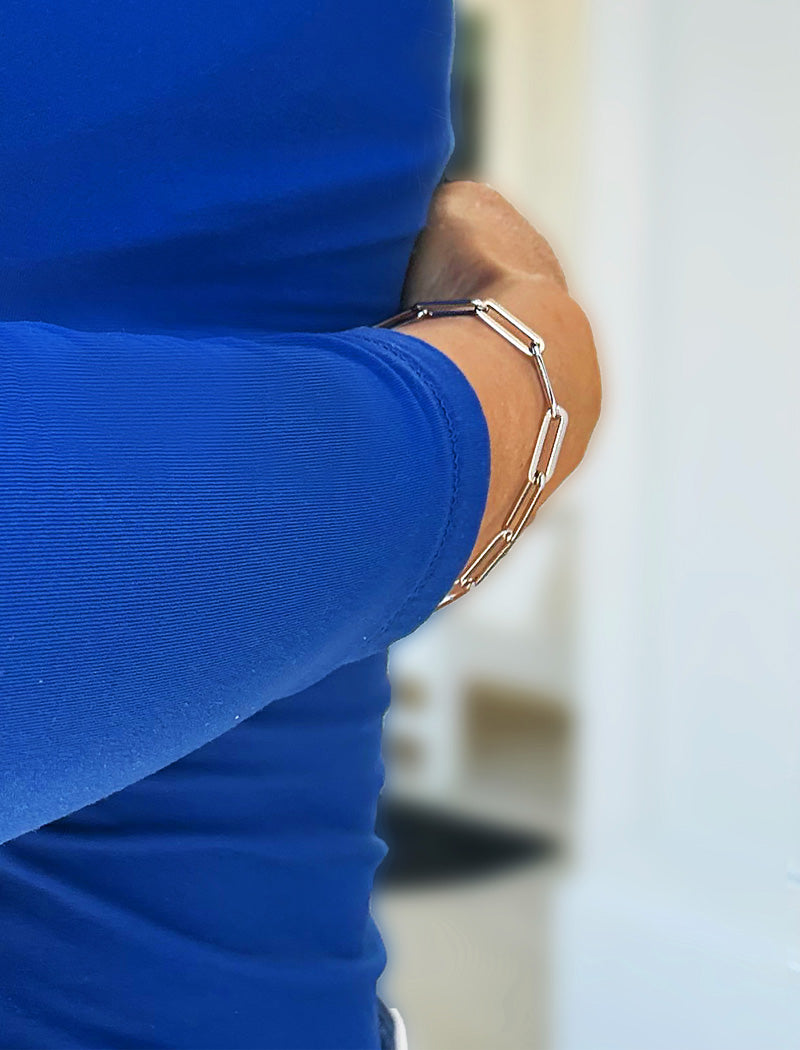 A close-up of a person wearing a stainless steel silver-toned geometric link bracelet on their wrist, paired with a bright blue ribbed long-sleeve top. Designed by AAPI celebrity jewelry designer SONIA HOU.