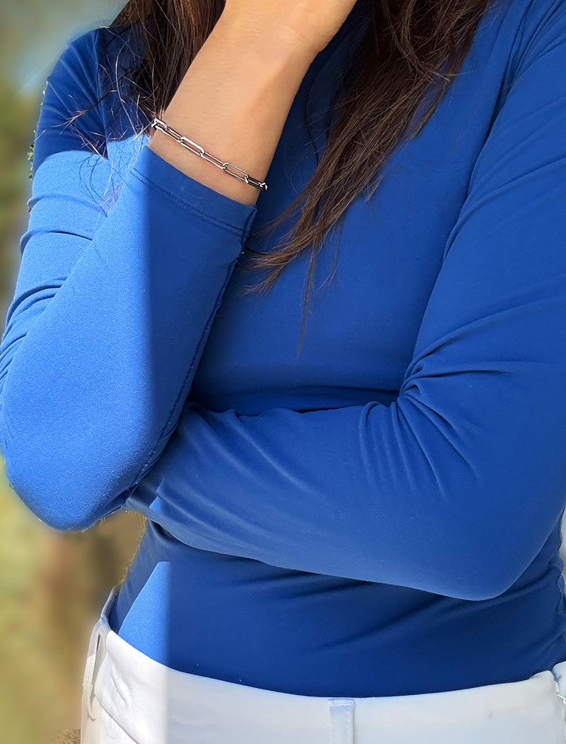A close-up of a person wearing a bright royal blue long-sleeve top and white pants, with a stainless steel silver chain bracelet on the wrist. Designed by AAPI celebrity jewelry designer SONIA HOU.