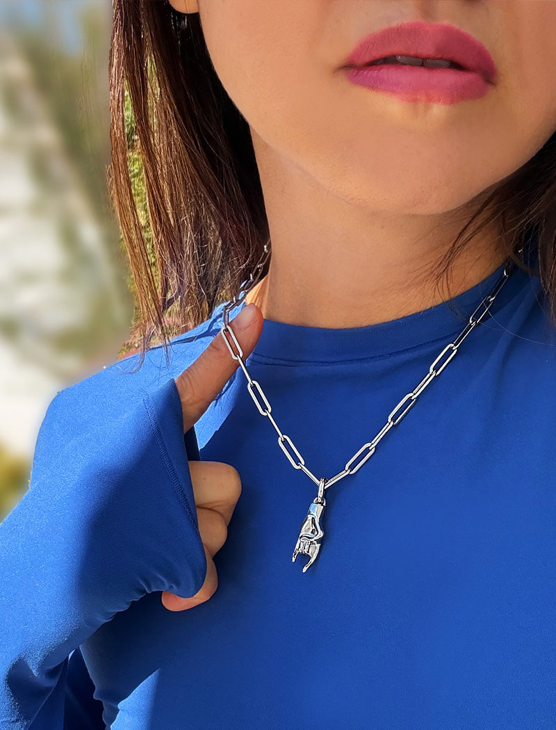 Person wearing a silver stainless steel Italian Hand pendant—also known as Mano Cornuta or the “Horned Hand” amulet.  Designed for everyone who values inclusivity, diversity, and meaning, it’s a timeless statement of strength and modern style. It's perfect for everyday wear. Designed by AAPI celebrity jewelry designer SONIA HOU.