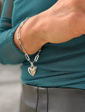 Sterling Silver bracelet with a heart-shaped pendant on a person wearing a teal top. Featuring a bold yet feminine Puffy Heart charm suspended from a sleek link chain, this bracelet radiates effortless confidence and charm. Designed to symbolize love, self-expression, and empowerment, the puffy heart serves as a daily reminder to lead with compassion and strength — for yourself and others. Designed by AAPI celebrity jewelry designer SONIA HOU.
