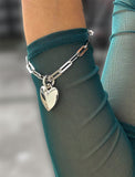 Sterling Silver bracelet with a heart-shaped pendant on a person wearing a teal top. Featuring a bold yet feminine Puffy Heart charm suspended from a sleek link chain, this bracelet radiates effortless confidence and charm. Designed to symbolize love, self-expression, and empowerment, the puffy heart serves as a daily reminder to lead with compassion and strength — for yourself and others. Designed by AAPI celebrity jewelry designer SONIA HOU.
