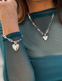 Sterling Silver bracelet with a heart-shaped pendant on a person wearing a teal top. Featuring a bold yet feminine Puffy Heart charm suspended from a sleek link chain, this bracelet radiates effortless confidence and charm. Designed to symbolize love, self-expression, and empowerment, the puffy heart serves as a daily reminder to lead with compassion and strength — for yourself and others. Designed by AAPI celebrity jewelry designer SONIA HOU.
