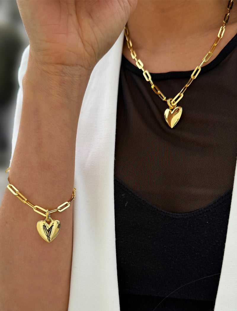 18K Gold vermeil chain necklace with a heart pendant worn by a person. Featuring a bold yet feminine Puffy Heart charm suspended from a sleek link chain, this bracelet radiates effortless confidence and charm. Designed to symbolize love, self-expression, and empowerment, the puffy heart serves as a daily reminder to lead with compassion and strength — Designed by AAPI celebrity jewelry designer SONIA HOU.
