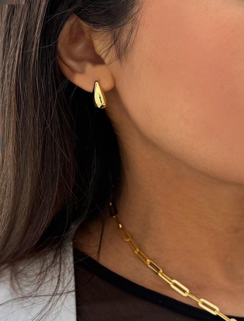 Close-up of a person wearing a gold earring and necklace. Delicately crafted from 18K gold and sterling silver, these modern Teardrop Earrings are more than a timeless accessory — they’re a symbol of strength, resilience, and beauty. The elegant teardrop shape captures life’s emotions with grace, turning a simple gesture into a statement of empowerment. Designed by AAPI celebrity jewelry designer SONIA HOU.
