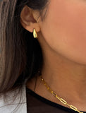 Close-up of a person wearing a gold earring and necklace. Delicately crafted from 18K gold and sterling silver, these modern Teardrop Earrings are more than a timeless accessory — they’re a symbol of strength, resilience, and beauty. The elegant teardrop shape captures life’s emotions with grace, turning a simple gesture into a statement of empowerment. Designed by AAPI celebrity jewelry designer SONIA HOU.
