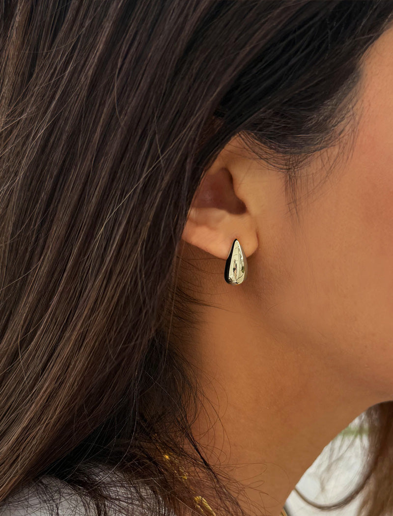 Close-up of an ear wearing a teardrop-shaped earring with a blurred background. Delicately crafted from sterling silver, these modern Teardrop Earrings are more than a timeless accessory — they’re a symbol of strength, resilience, and beauty. The elegant teardrop shape captures life’s emotions with grace, turning a simple gesture into a statement of empowerment. Designed by AAPI celebrity jewelry designer SONIA HOU.
