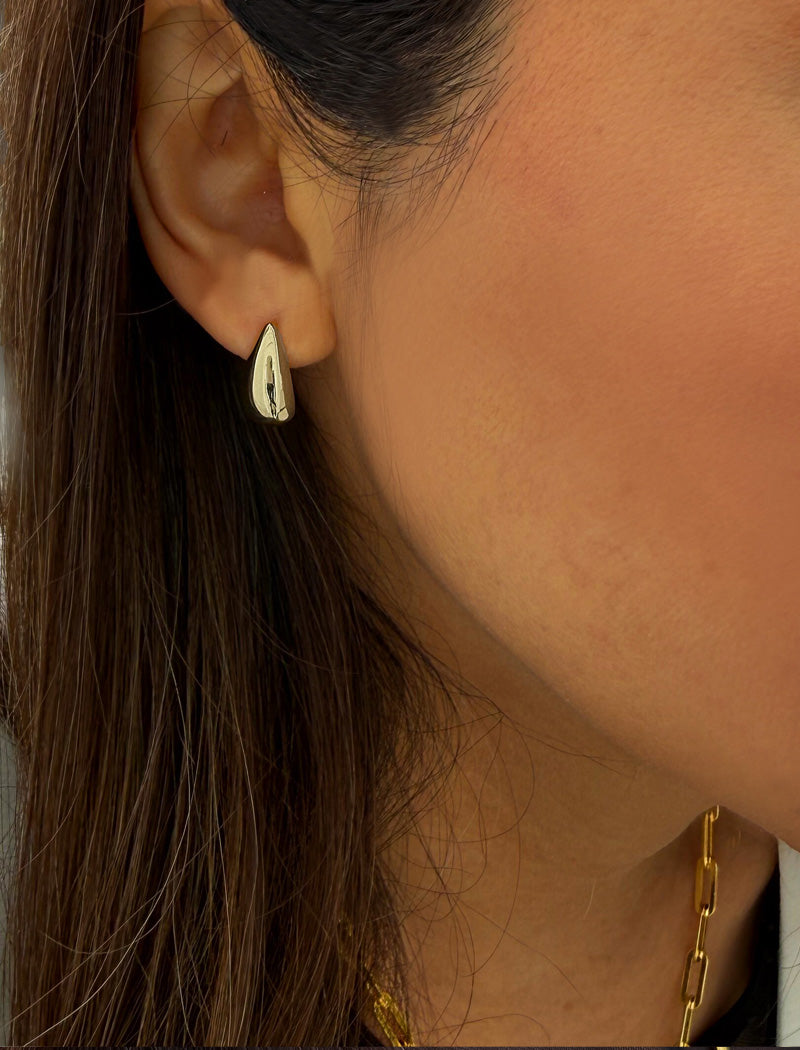 Close-up of a person wearing a silver earring with a neutral background. Delicately crafted from sterling silver, these modern Teardrop Earrings are more than a timeless accessory — they’re a symbol of strength, resilience, and beauty. The elegant teardrop shape captures life’s emotions with grace, turning a simple gesture into a statement of empowerment. Designed by AAPI celebrity jewelry designer SONIA HOU.