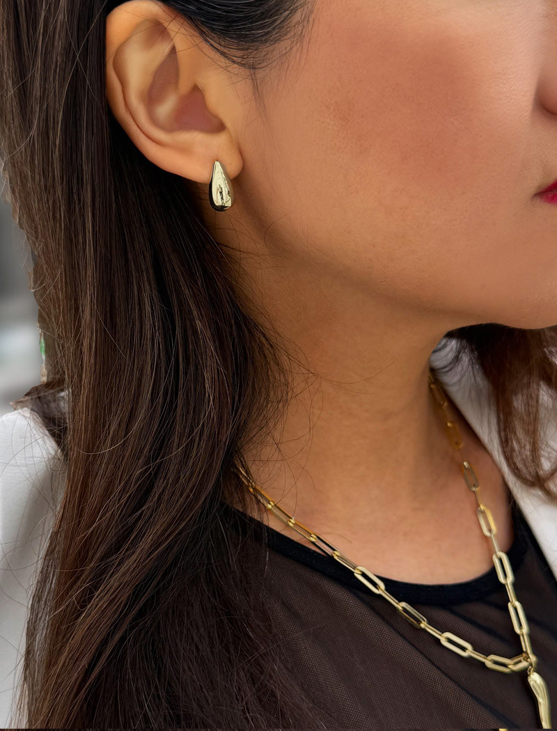 Close-up of a person wearing silver earrings and a necklace. Delicately crafted from sterling silver, these modern Teardrop Earrings are more than a timeless accessory — they’re a symbol of strength, resilience, and beauty. The elegant teardrop shape captures life’s emotions with grace, turning a simple gesture into a statement of empowerment. Designed by AAPI celebrity jewelry designer SONIA HOU.