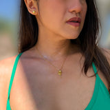 A close-up lifestyle shot of a woman wearing a delicate gold tennis racquet and ball pendant necklace and a matching gold tennis ball stud earring. The pendant features a stylized sun or flower design. Designed by Sonia Hou, a celebrity AAPI inclusive demi-fine jewelry designer. Available in 18K Gold Over Sterling Silver, Sterling Silver and 18K Gold PVD Sterling Silver (Waterproof).
