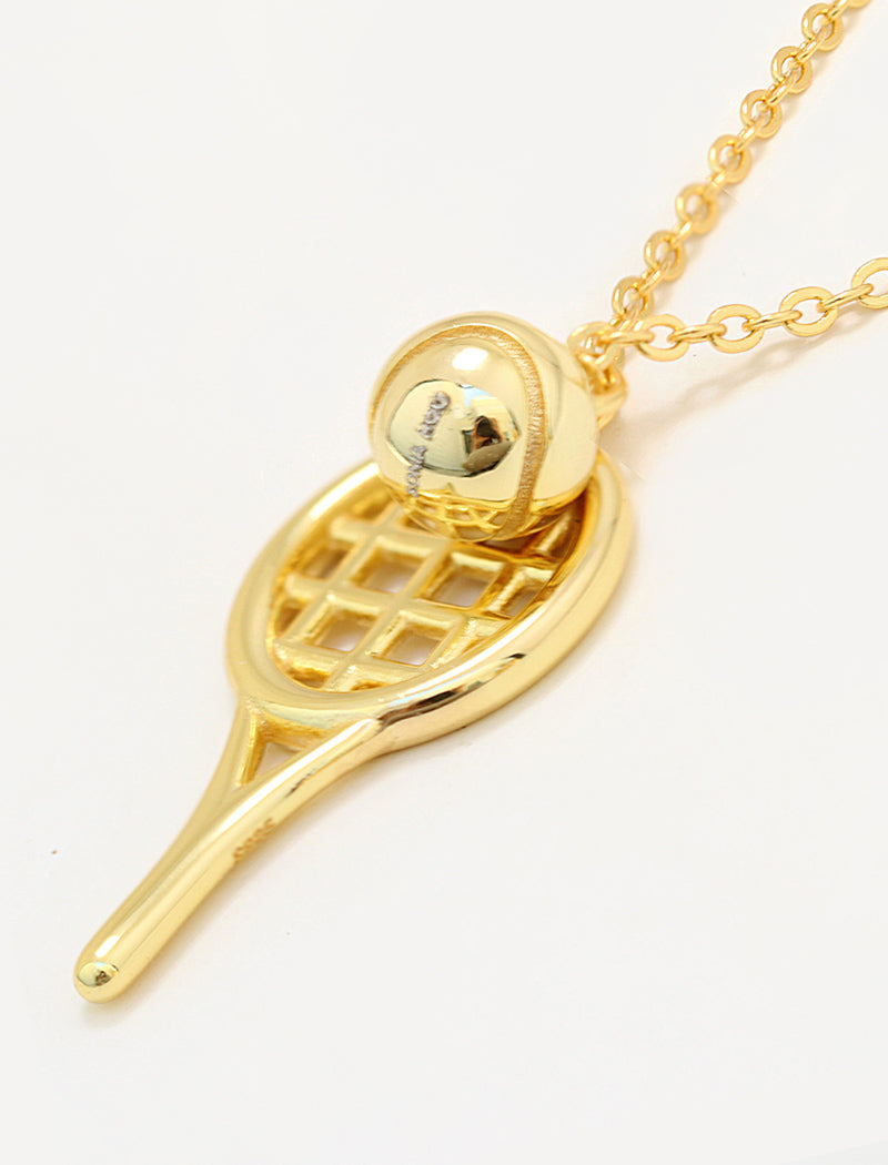 A gold tennis racket pendant necklace with a small gold tennis ball charm resting on the racket head, shown on a clean white background by Sonia Hou, a celebrity AAPI inclusive demi-fine jewelry designer. Available in 18K Gold Over Sterling Silver, Sterling Silver and 18K Gold PVD Stainless Steel (Waterproof).