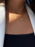 A close-up of a model wearing a delicate gold tennis ball racket pendant necklace, styled with a white blazer and black top. Designed by Sonia Hou, a celebrity AAPI inclusive demi-fine jewelry designer. Available in 18K Gold Over Sterling Silver, Sterling Silver and 18K Gold PVD Sterling Silver (Waterproof).
