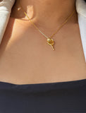 A close-up of a person's neck and chest wearing a delicate gold tennis racket pendant necklace with a tennis ball detail, styled with a white collared shirt and a dark navy top. Designed by Sonia Hou, a celebrity AAPI inclusive demi-fine jewelry designer. Available in 18K Gold Over Sterling Silver, Sterling Silver and 18K Gold PVD Sterling Silver.