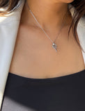 A close-up of a model wearing a delicate silver chain necklace with a tennis ball racket pendant, styled with a black top and a light-colored blazer. Designed by Sonia Hou, a celebrity AAPI inclusive demi-fine jewelry designer. Available in 18K Gold Over Sterling Silver, Sterling Silver and 18K Gold PVD Sterling Silver (Waterproof).
