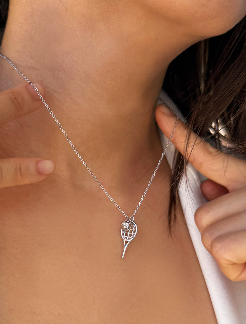 A close-up of a person's neck and chest wearing a delicate silver chain necklace with a tennis ball racket-shaped pendant. Designed by Sonia Hou, a celebrity AAPI inclusive demi-fine jewelry designer. Available in 18K Gold Over Sterling Silver, Sterling Silver and 18K Gold PVD Sterling Silver (Waterproof).
