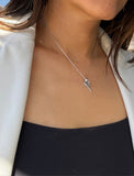 A close-up of a person wearing a delicate silver tennis racquet ball chain necklace with a small tennis ball pendant, styled with a white blazer and black top. Designed by Sonia Hou, a celebrity AAPI inclusive demi-fine jewelry designer. Available in 18K Gold Over Sterling Silver, Sterling Silver and 18K Gold PVD Sterling Silver (Waterproof).