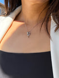 A close-up of a person wearing a delicate silver tennis racquet ball necklace featuring a tiny dangling tennis ball, styled with a black top and a light beige blazer. Designed by Sonia Hou, a celebrity AAPI inclusive demi-fine jewelry designer. Available in 18K Gold Over Sterling Silver, Sterling Silver and 18K Gold PVD Sterling Silver (Waterproof).