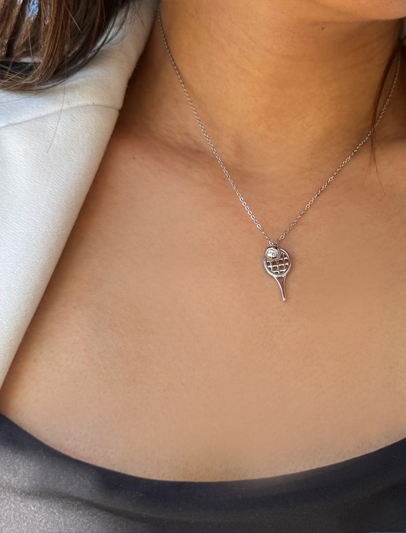 A close-up of a person's neck and chest wearing a delicate silver chain necklace with a tennis ball racket pendant. Designed by Sonia Hou, a celebrity AAPI inclusive demi-fine jewelry designer. Available in 18K Gold Over Sterling Silver, Sterling Silver and 18K Gold PVD Sterling Silver (Waterproof).
